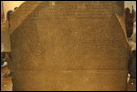 Розеттский камень. Гранодиорит, Рашид, 196 г. до Р.Х. Британский музей. EA 24. Плита из гранодиорита, найденная в 1799 г. в Египте возле небольшого города Розетта (теперь Рашид), недалеко от Александрии, с выбитыми на ней тремя идентичными по смыслу текстами, два из них — на древнеегипетском языке: начертанными древнеегипетскими иероглифами и египетским демотическим письмом (которое представляет собой сокращённую скоропись эпохи позднего Египта), третий —на древнегреческом языке. Древнегреческий был хорошо известен лингвистам, и сопоставление трёх текстов данной надписи послужило отправной точкой для расшифровки египетских иероглифов. Тексты представляют собой благодарность, которую в 196 г. до Р.Х. египетские жрецы адресовали Птолемею V Эпифану, монарху из династии Птолемеев. Начало надписи: "Новому царю, получившему царство от отца..." В эллинистический период многие подобные документы в пределах греческой ойкумены распространялись в виде дву- или триязычных текстов. Камень был обнаружен 15 июля 1799 г. капитаном французских войск в Египте Пьером-Франсуа Бушаром при сооружении форта Сен-Жюльен близ Розетты на западном рукаве дельты Нила. Офицер понял важность находки и отправил камень в Каир, где за год до этого по приказу Наполеона был открыт Институт Египта. В 1801 г. французы потерпели в Африке поражение от англичан и были вынуждены передать им артефакт вместе с рядом других памятников. Розеттский камень имеет высоту 114,4 см, ширину 72,3 см и толщину 27,9 см. Он весит примерно 760 кг. Передняя поверхность полированная с вырезанными надписями на ней. Обратная сторона грубо обработана. Камень является фрагментом большой стелы. При последующих поисках никаких дополнительных фрагментов не было найдено. Из-за повреждений ни один из трёх текстов не является абсолютно полным. Греческий текст содержит 54 строки, из которых первые 27 сохранились в полном объёме, а остальные частично утрачены в связи с диагональным отколом в правом нижнем углу камня. Демотический текст сохранился лучше остальных: это 32 стоки, из которых у 14 первых слегка повреждена правая сторона. Иероглифический текст пострадал больше всего. Сохранились только последние 14 строк иероглифического текста, все они отколоты на правой стороне, 12 — на левой.