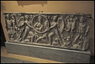 Стенка саркофага. Мрамор. Рим. Конец III в. Эрмитаж. А 1126. В центре — изображение умершей в медальоне, который поддерживают два Эрота. По сторонам — два гения плодородия.